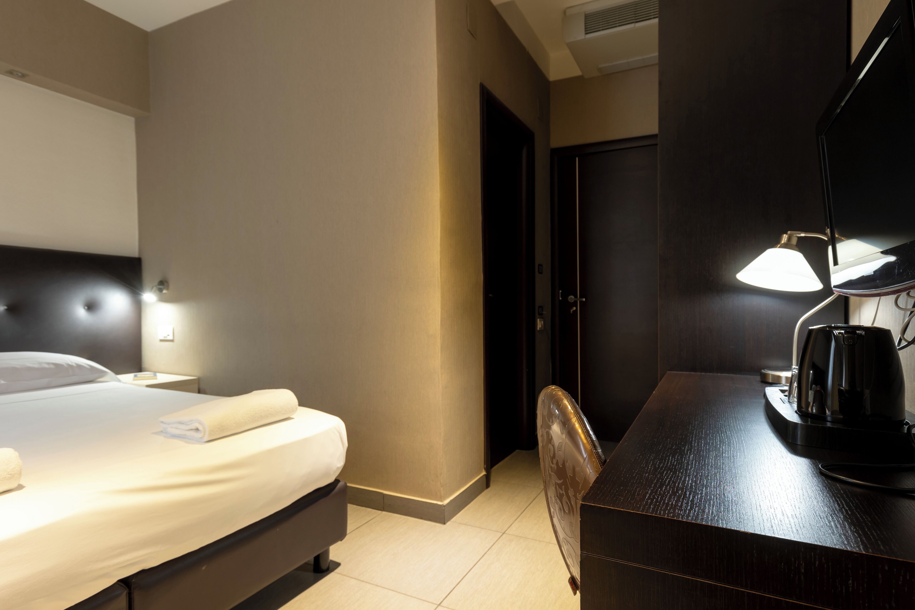 Una habitación de hotel con cama, mesita de noche, lámpara y escritorio con silla.