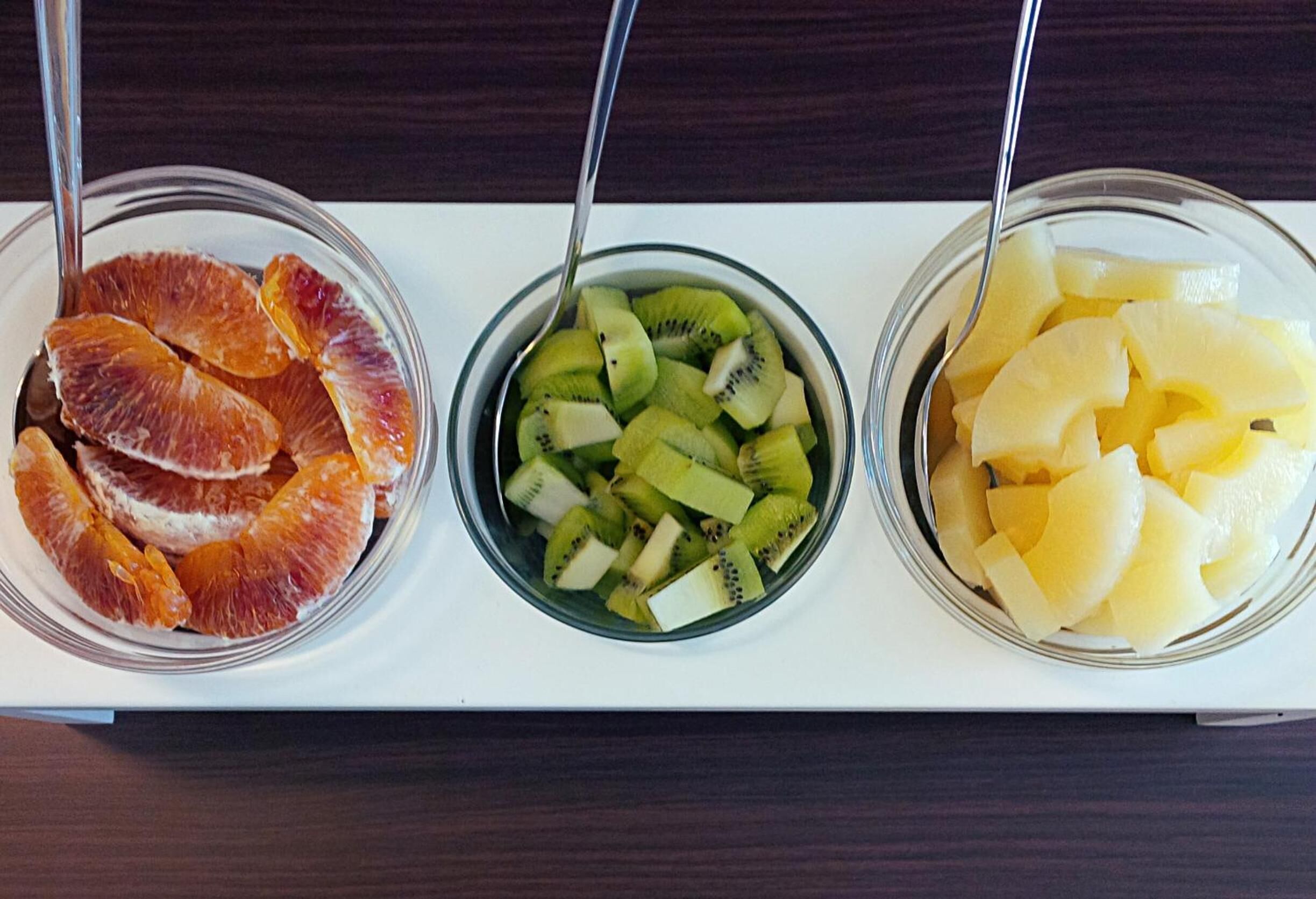Three bowls of fruit on a white tray.