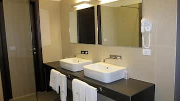 A modern bathroom with two sinks, a large mirror, a hairdryer, and towels hanging on the wall.
