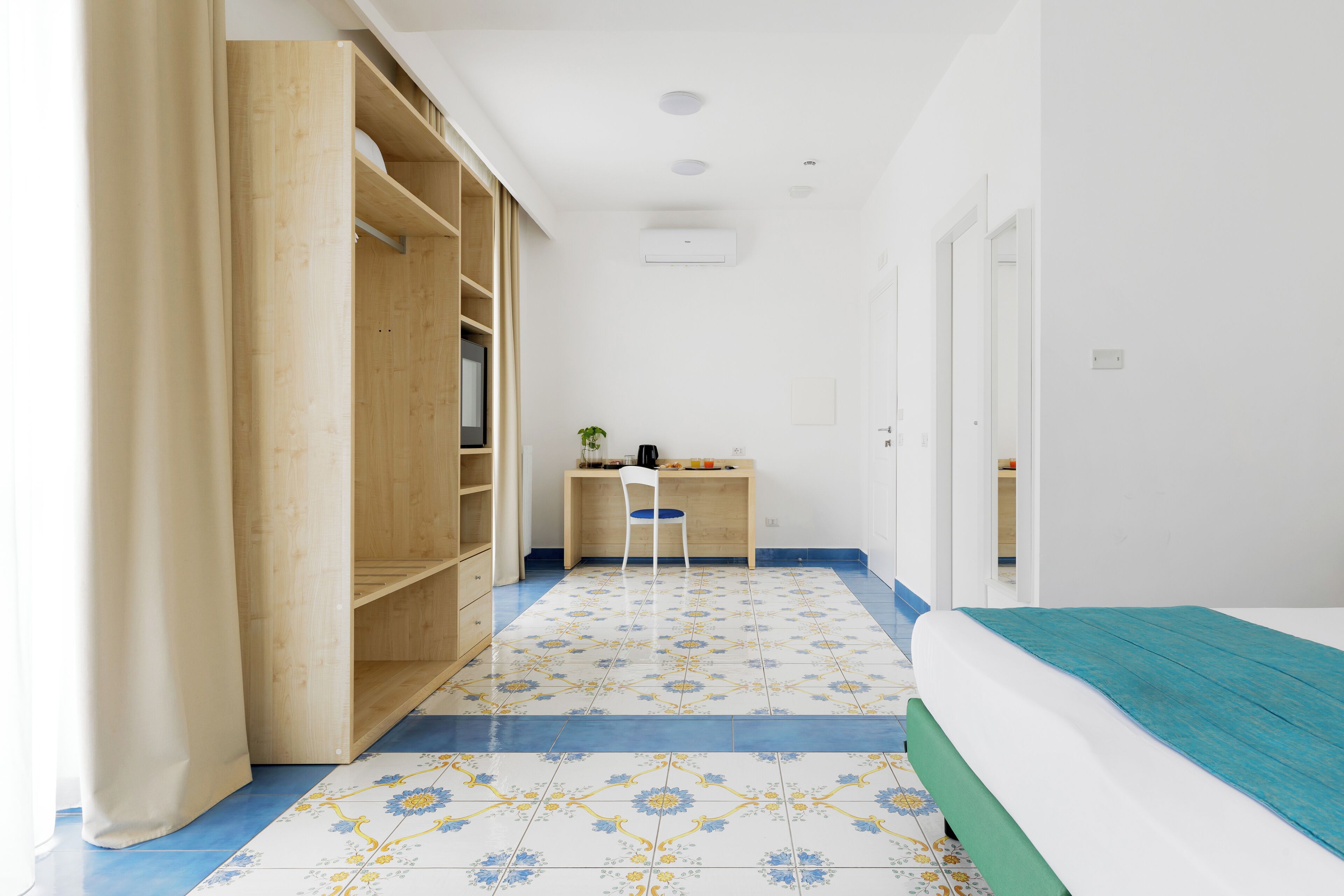 A bedroom with a bed, a desk, and a chair. There is a wardrobe and a door leading to another room.