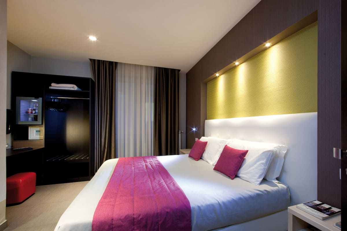 A modern hotel room with a large bed, a bedside table, a TV, and a wardrobe.