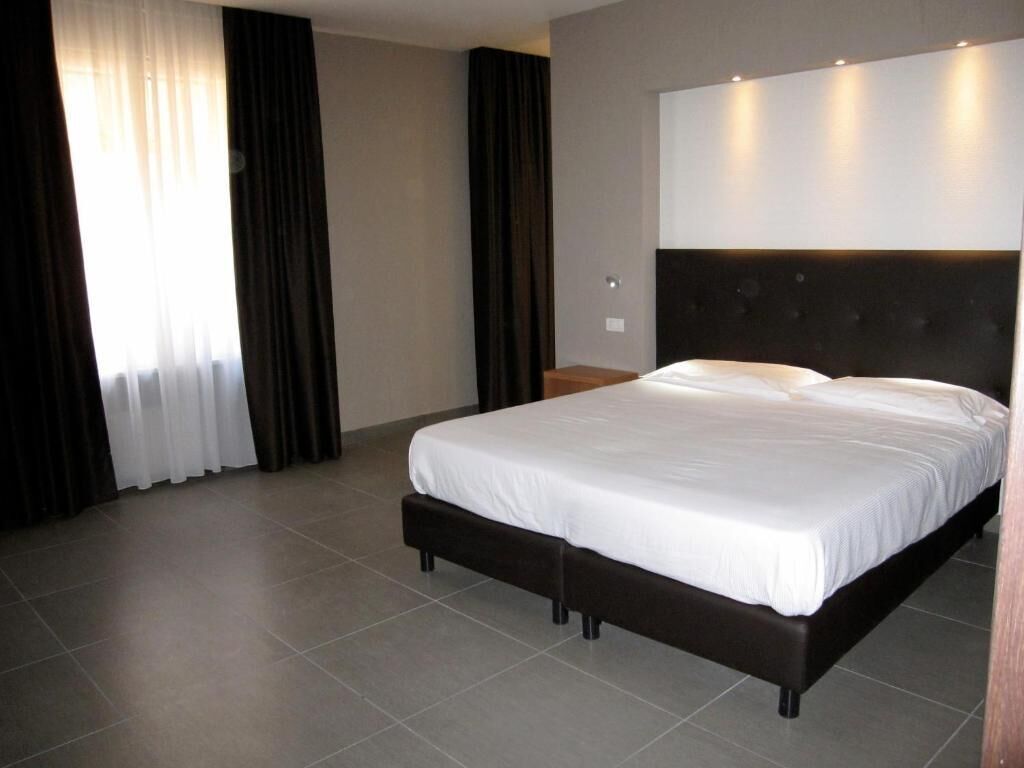 A modern hotel room with a large bed, dark headboard, and a neutral color scheme.