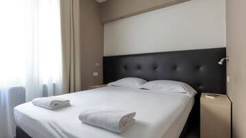 A neatly made bed with white linens and two folded towels, a dark headboard, and a small bedside table with a book.