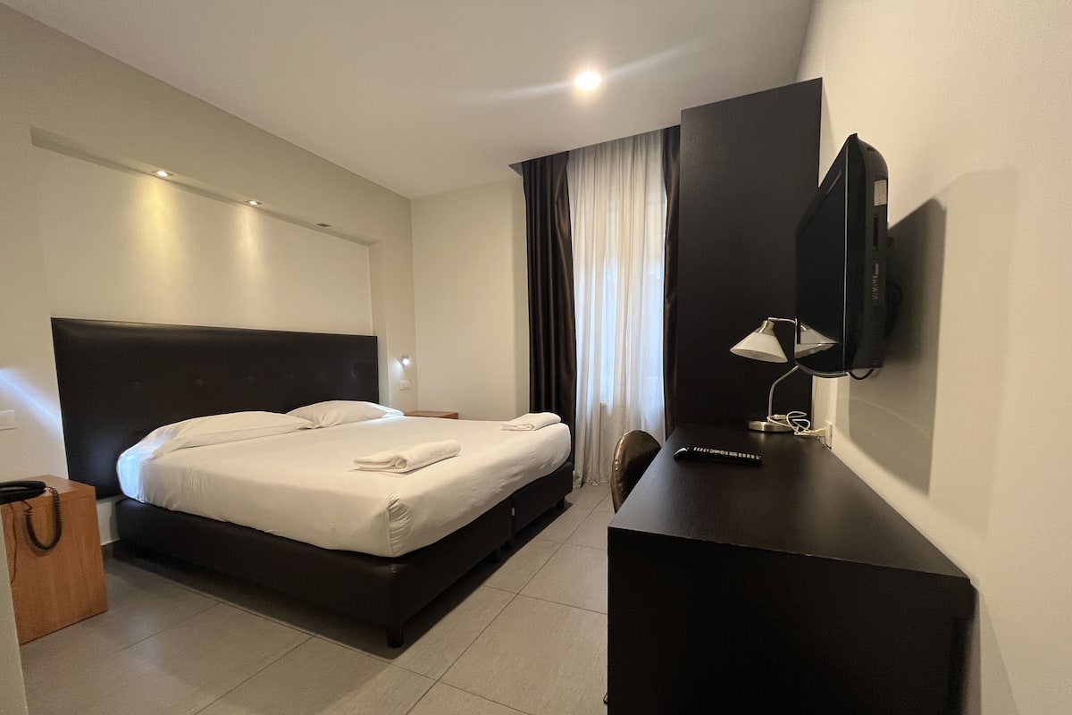 A hotel room with a bed, a desk, a TV, and a window with curtains.