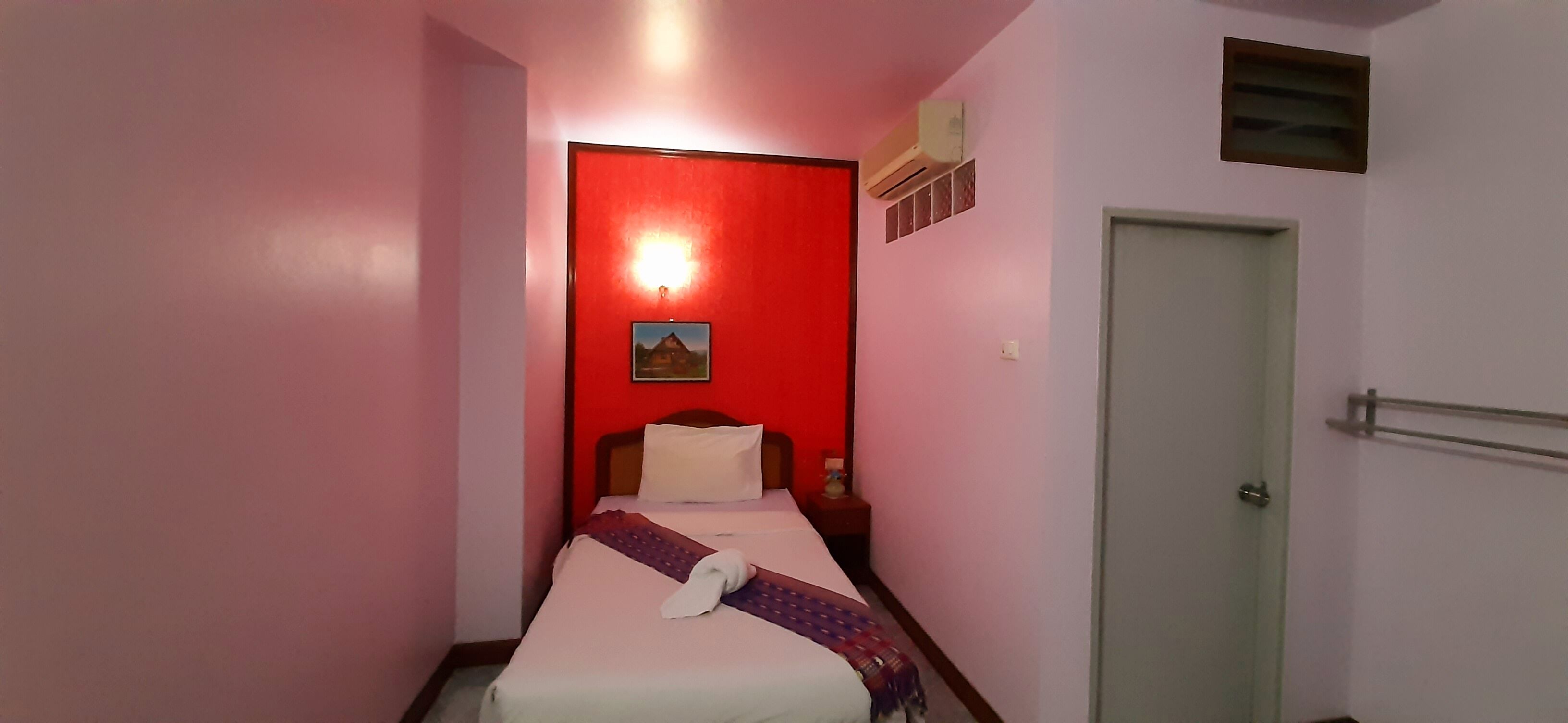 Une chambre d’hôtel avec un lit, une table de chevet, un climatiseur fixé au mur et une porte.