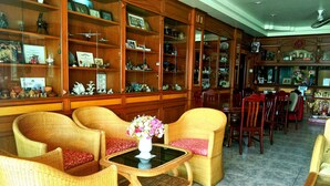 A spacious room with wicker furniture, a glass-top table with a vase of flowers, and wooden shelves filled with various items. - Thepparat Lodge Krabi (Krabi)