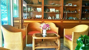 A room with wicker furniture, a glass display cabinet with collectibles, and a large window. - Thepparat Lodge Krabi (Krabi)
