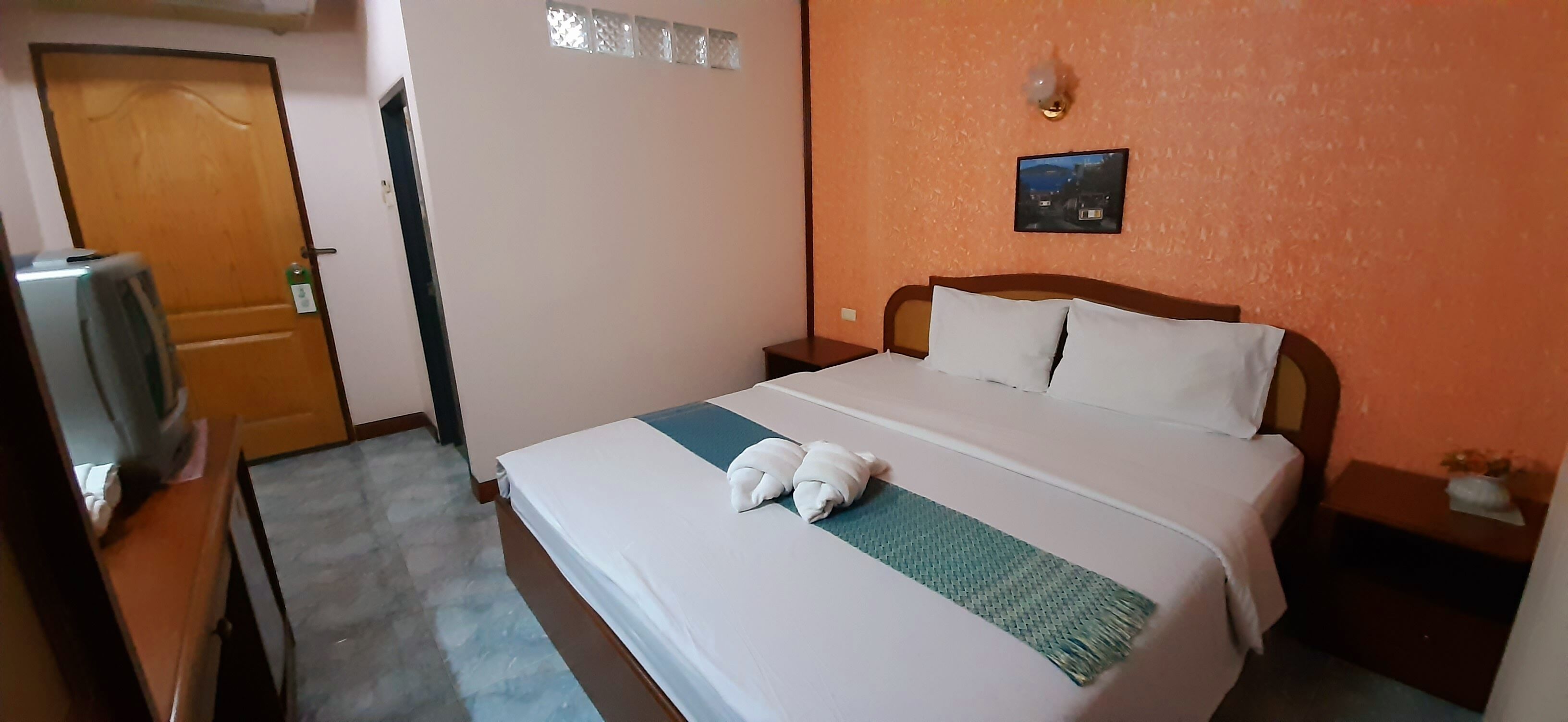 Una habitación de hotel con una cama, una mesita de noche, un televisor montado en la pared y una puerta.