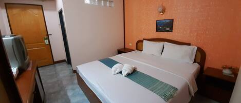 Una habitación de hotel con una cama, una mesita de noche, un televisor montado en la pared y una puerta.