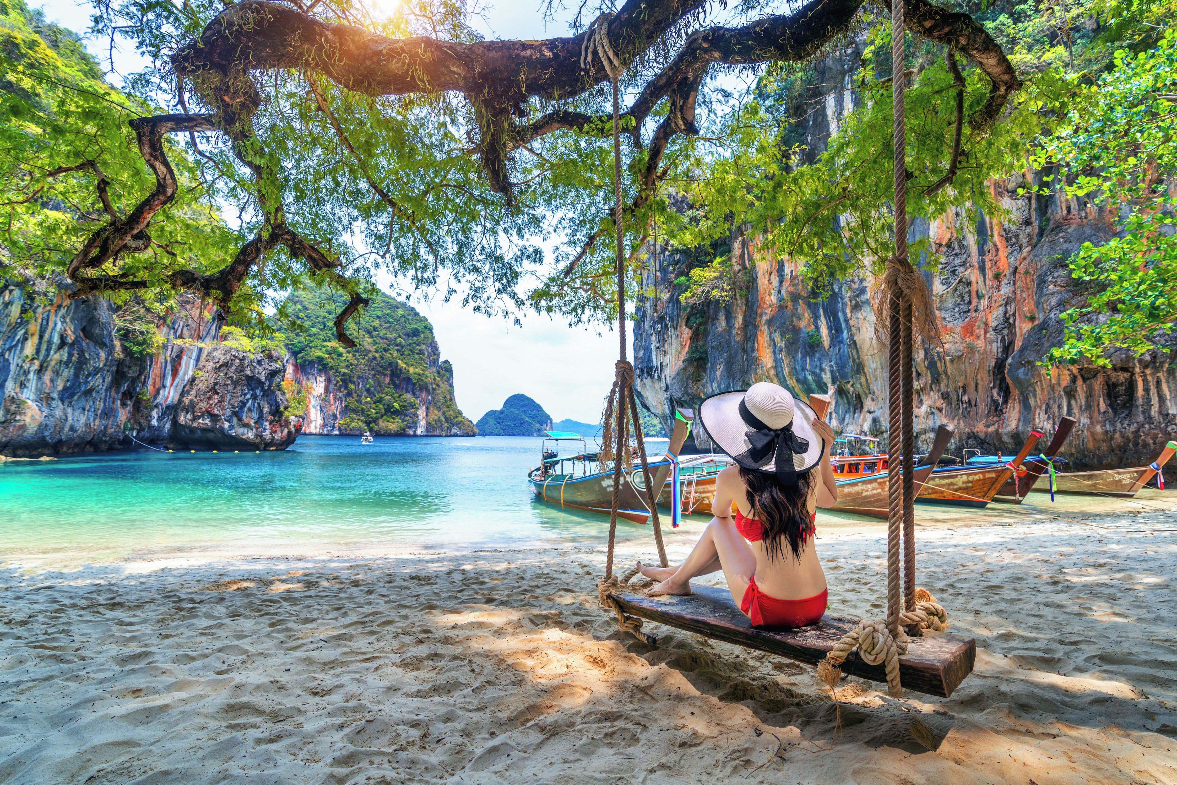 A beach with a swing, boats, and rocky cliffs.