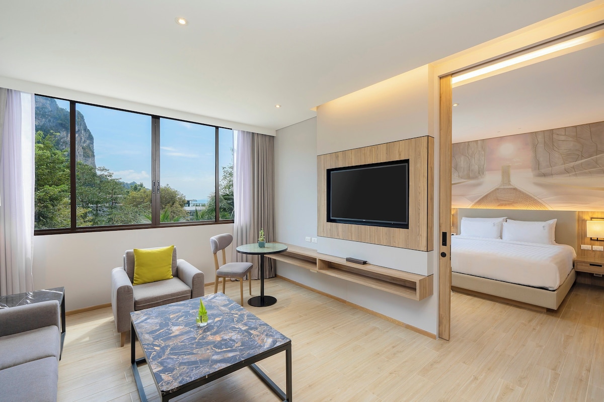 Une chambre d’hôtel moderne dotée d’une grande télévision, d’un lit, d’un canapé, d’une table à manger et offrant une vue sur l’extérieur.