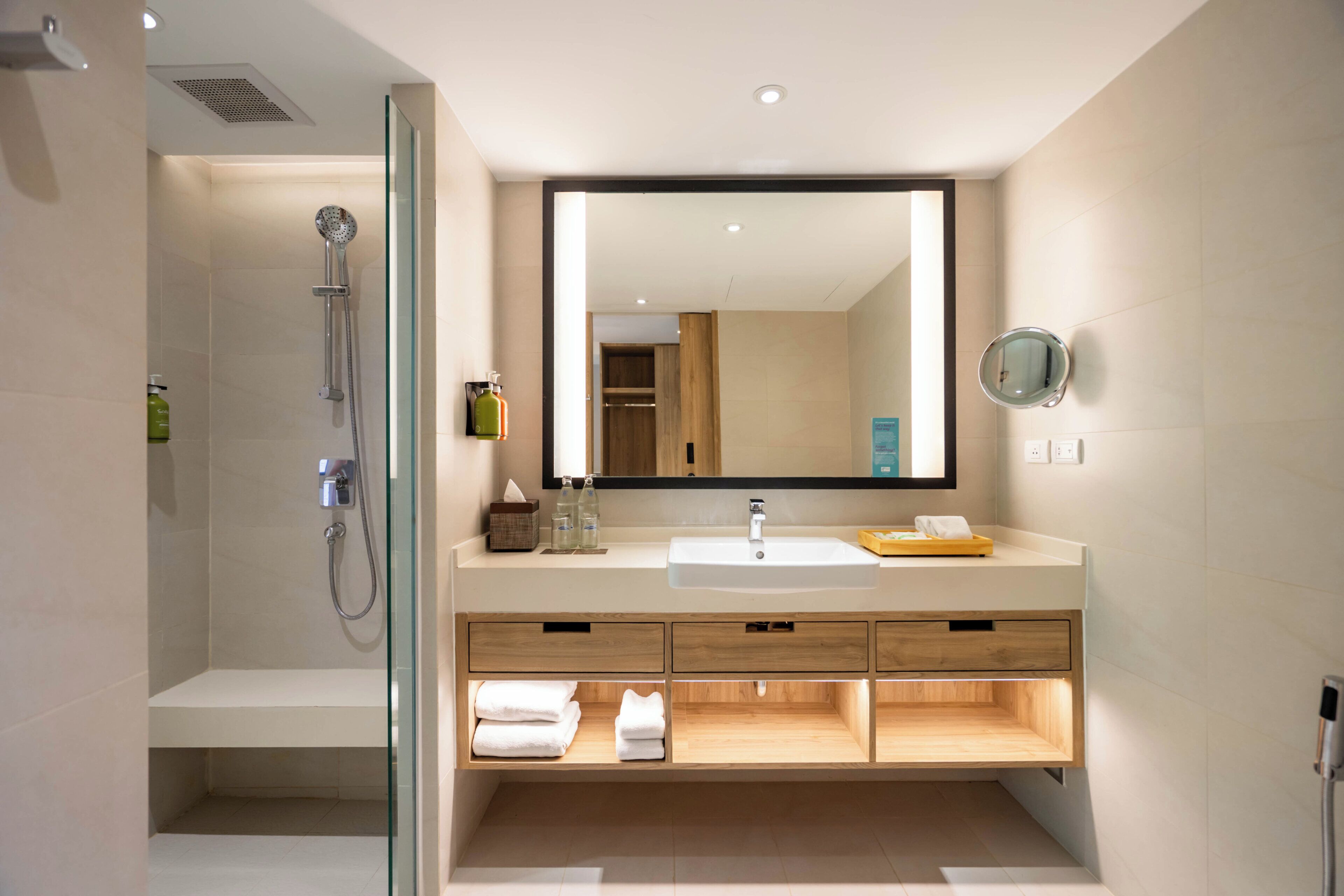 Een moderne badkamer met een douchecabine van glas, een grote spiegel en een houten wastafelmeubel met lades.