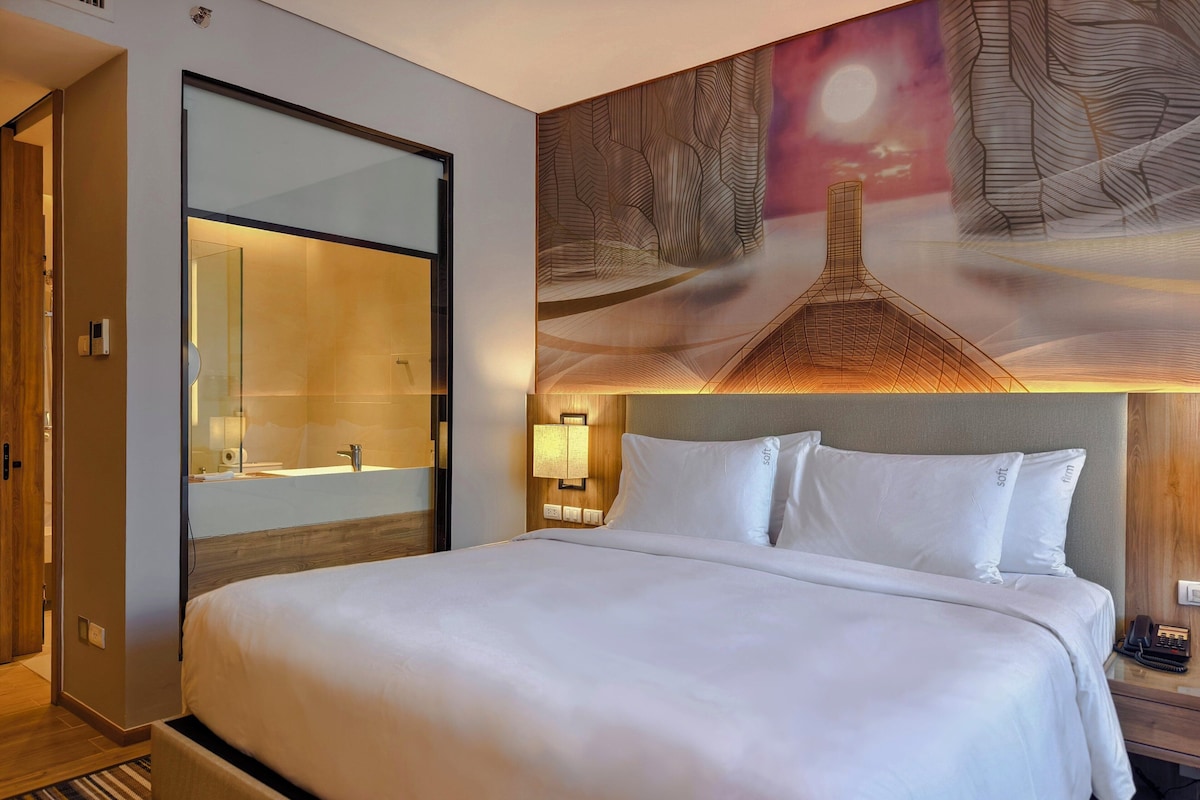 Une chambre d’hôtel avec un grand lit, une salle de bain dotée d’une paroi en verre et un mur décoré d’une fresque.