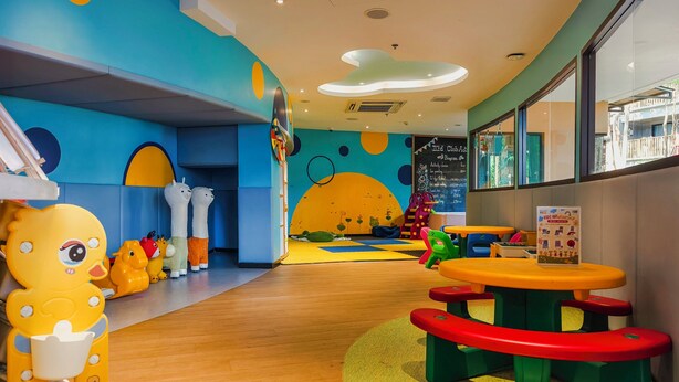 Un espace de jeux pour enfants avec des jouets colorés, un tapis de jeu et une table avec des tabourets.