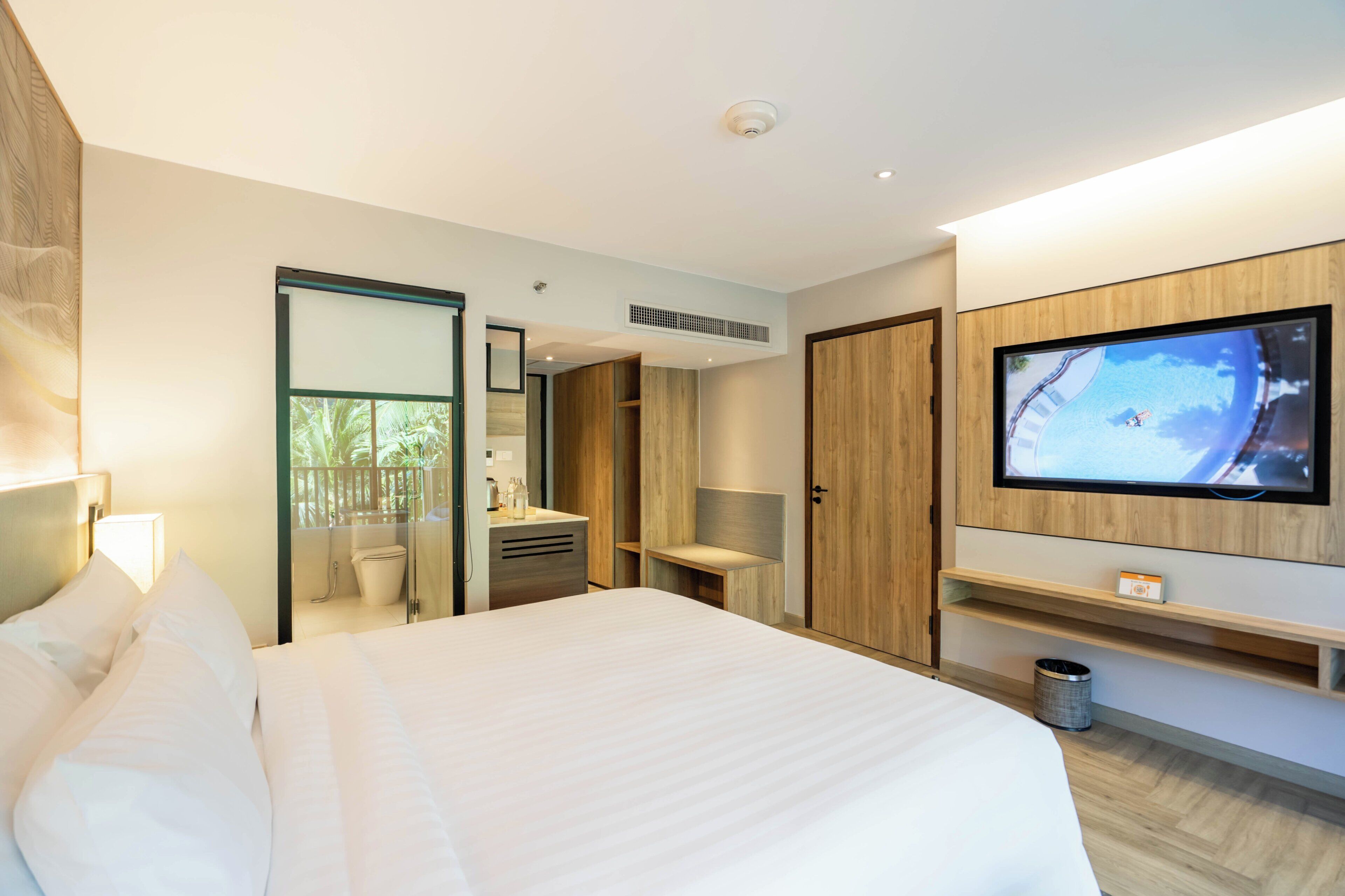 A modern hotel room with a large bed, a television, a bathroom, and a wooden wardrobe.