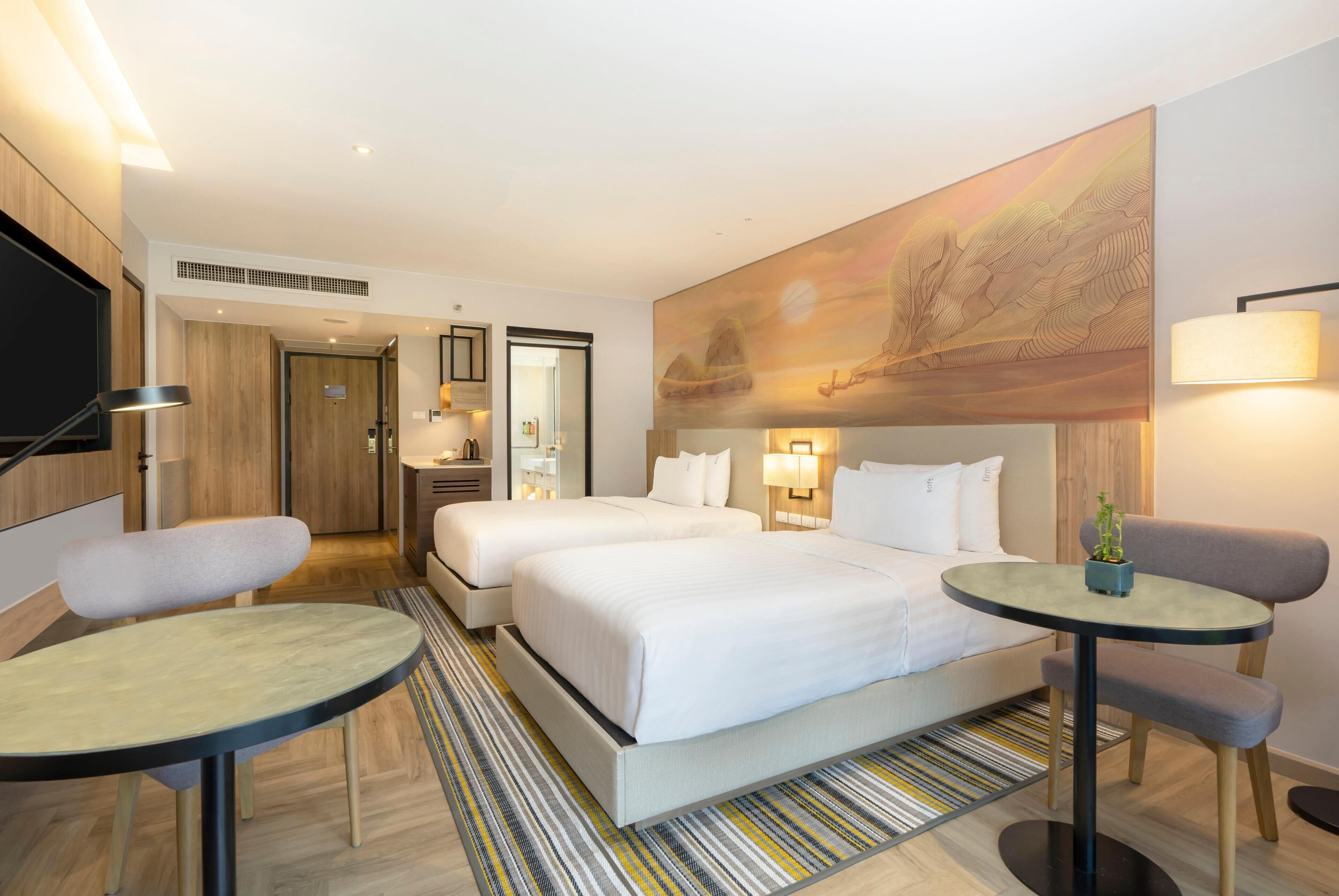 A hotel room with two beds, a small round table, a chair, a TV, and a painting on the wall.