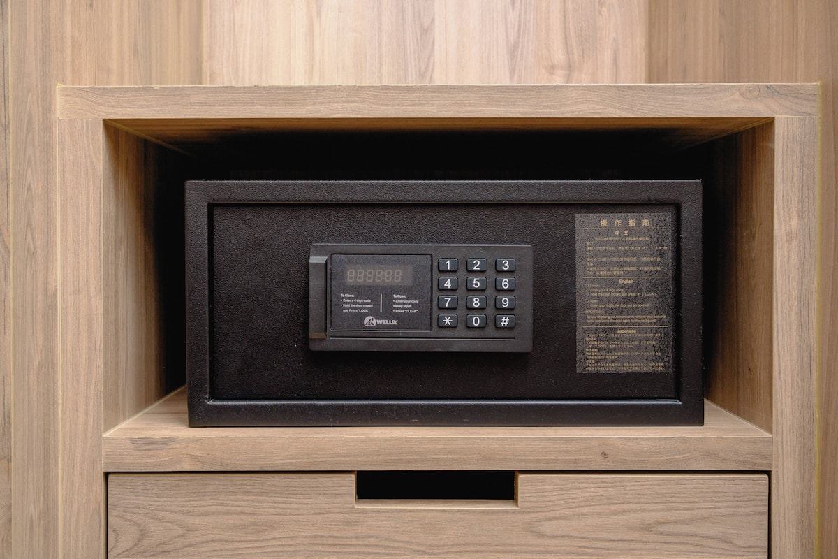 Una caja fuerte negra con teclado y pantalla, ubicada en un mueble de madera con un cajón debajo.