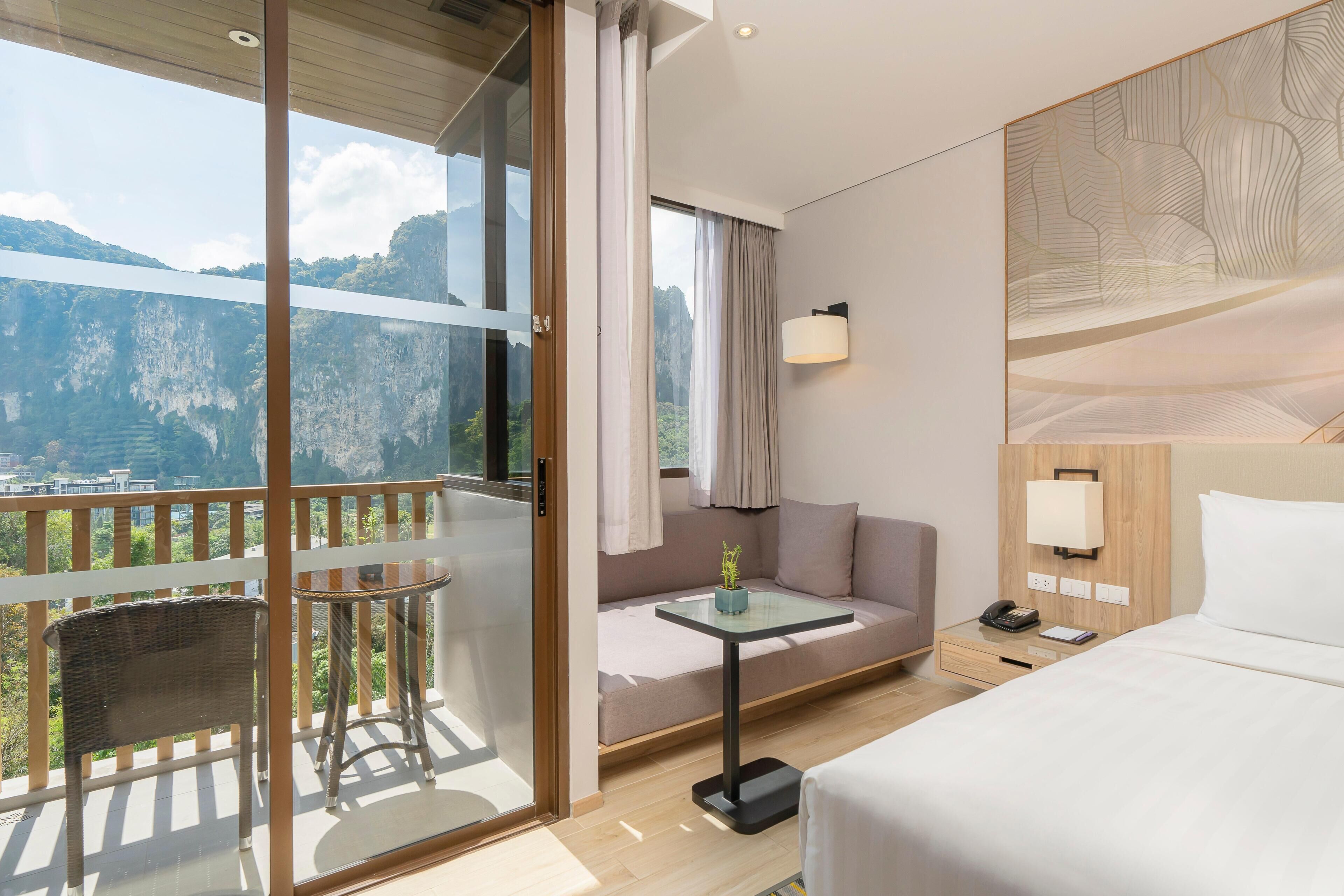 A hotel room with a balcony, a sofa, a bed, a nightstand, and a table.