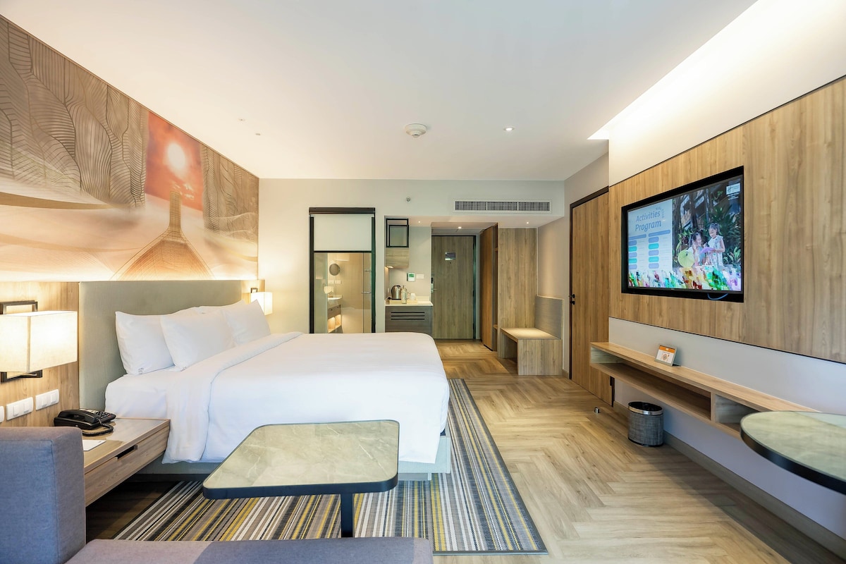 Une chambre d’hôtel moderne avec un grand lit, une table de chevet, une lampe, une télévision et un petit coin salon.
