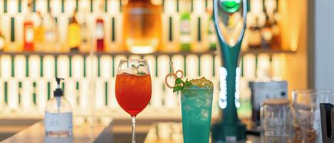 Um balcão de bar com duas bebidas, um frasco de álcool em gel e uma ferramenta de bar verde.
