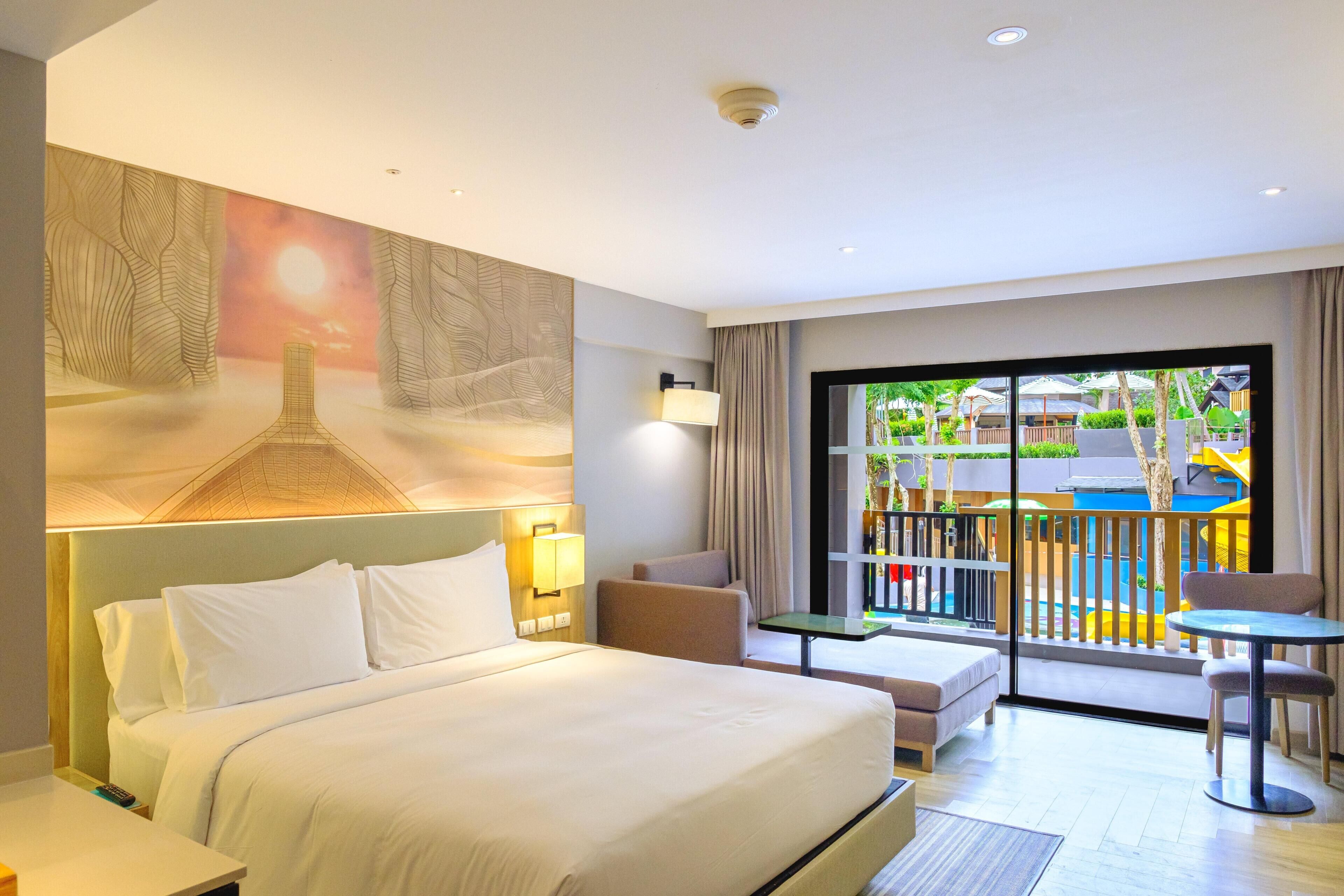 A hotel room with a large bed, a balcony with a view, a seating area, and a wall mural.