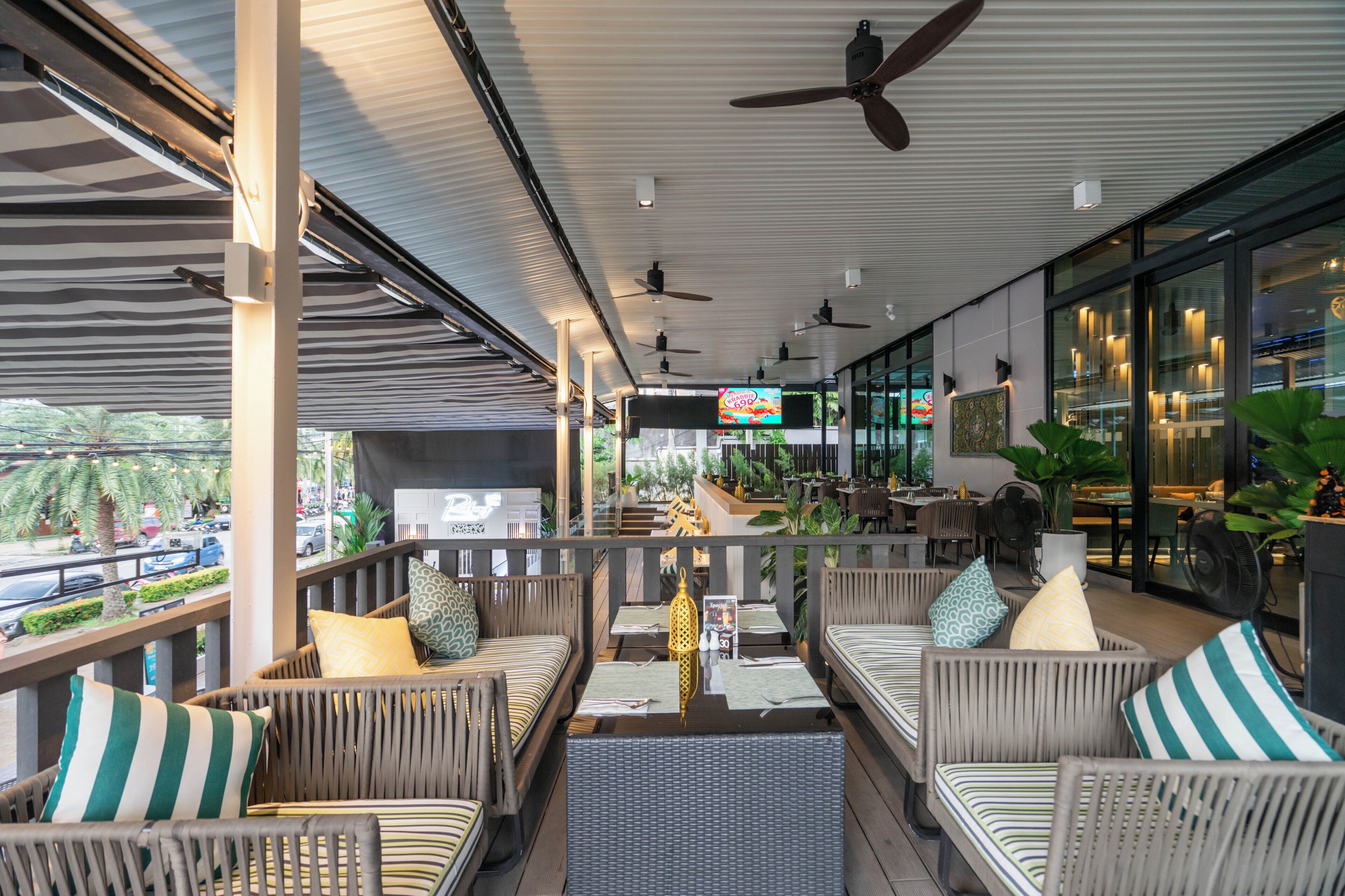 An outdoor seating area with wicker furniture, ceiling fans, and a view of the street.