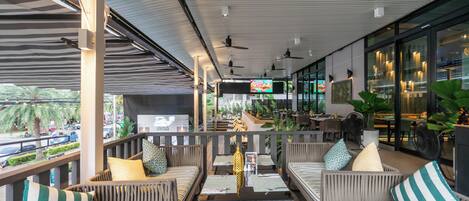 An outdoor seating area with wicker furniture, ceiling fans, and a view of the street.