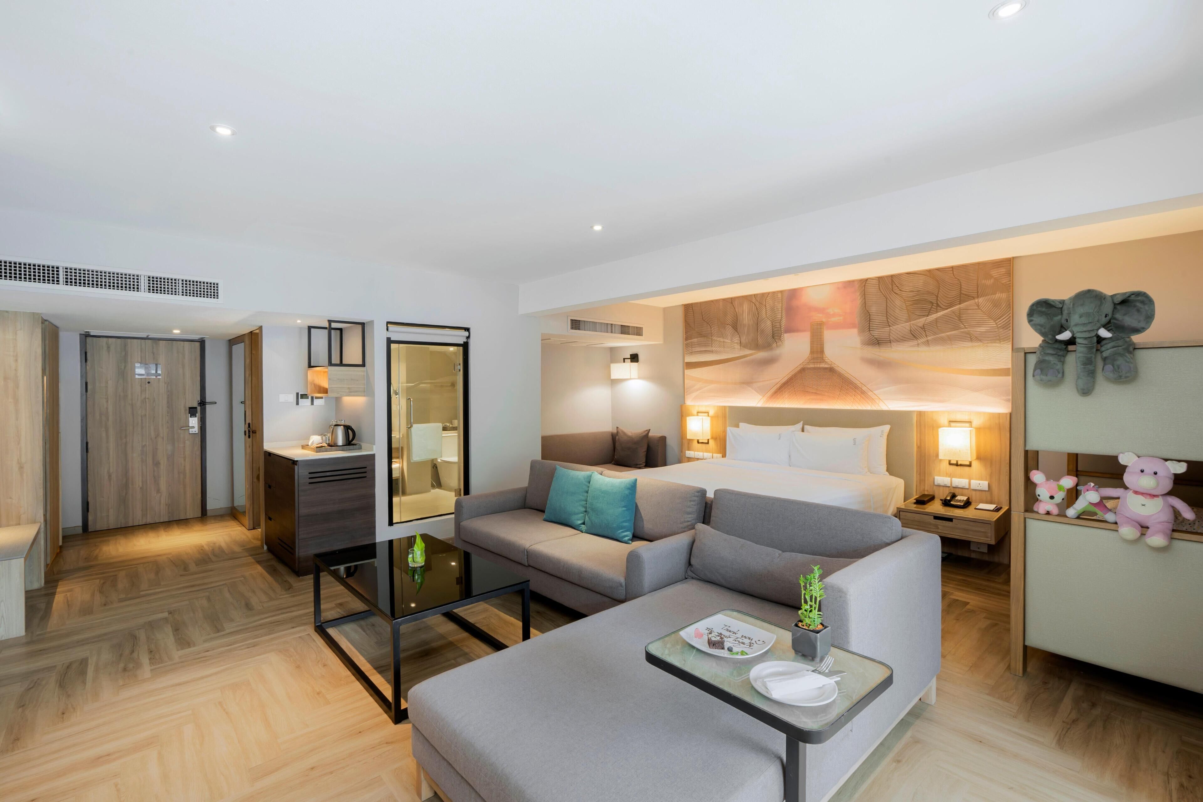 A modern hotel room with a sofa, a dining table, a bed, and a wall-mounted TV.