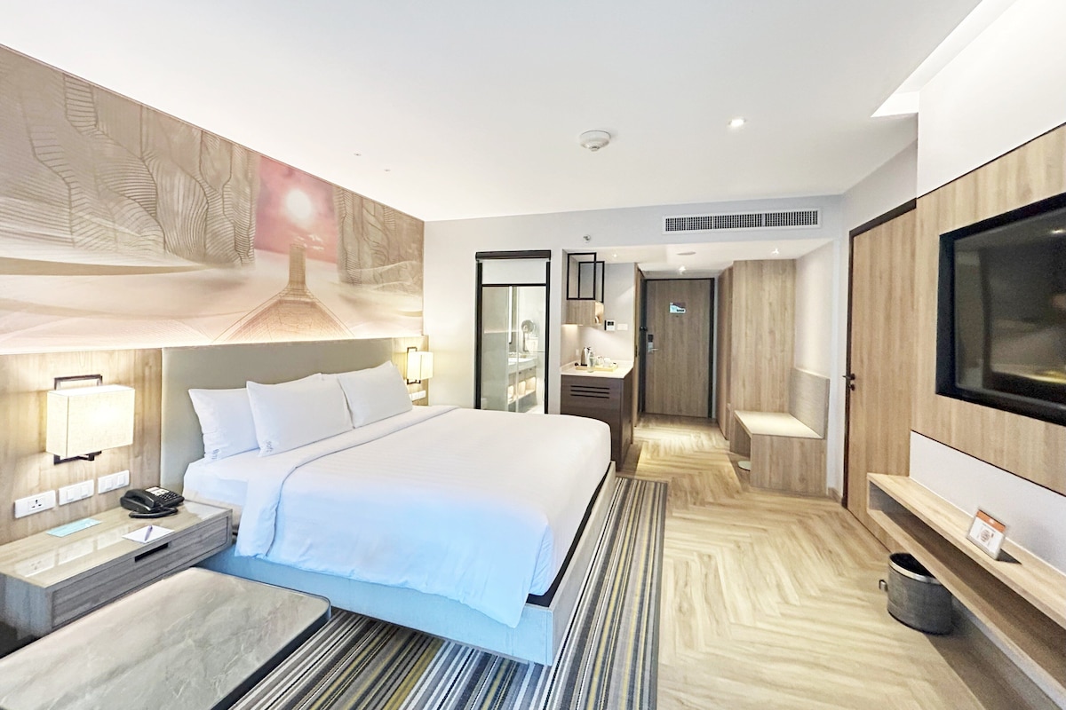 Une chambre d’hôtel moderne dotée d’un grand lit, de tables de chevet, d’une télévision et d’une salle de bain avec un miroir et un lavabo.
