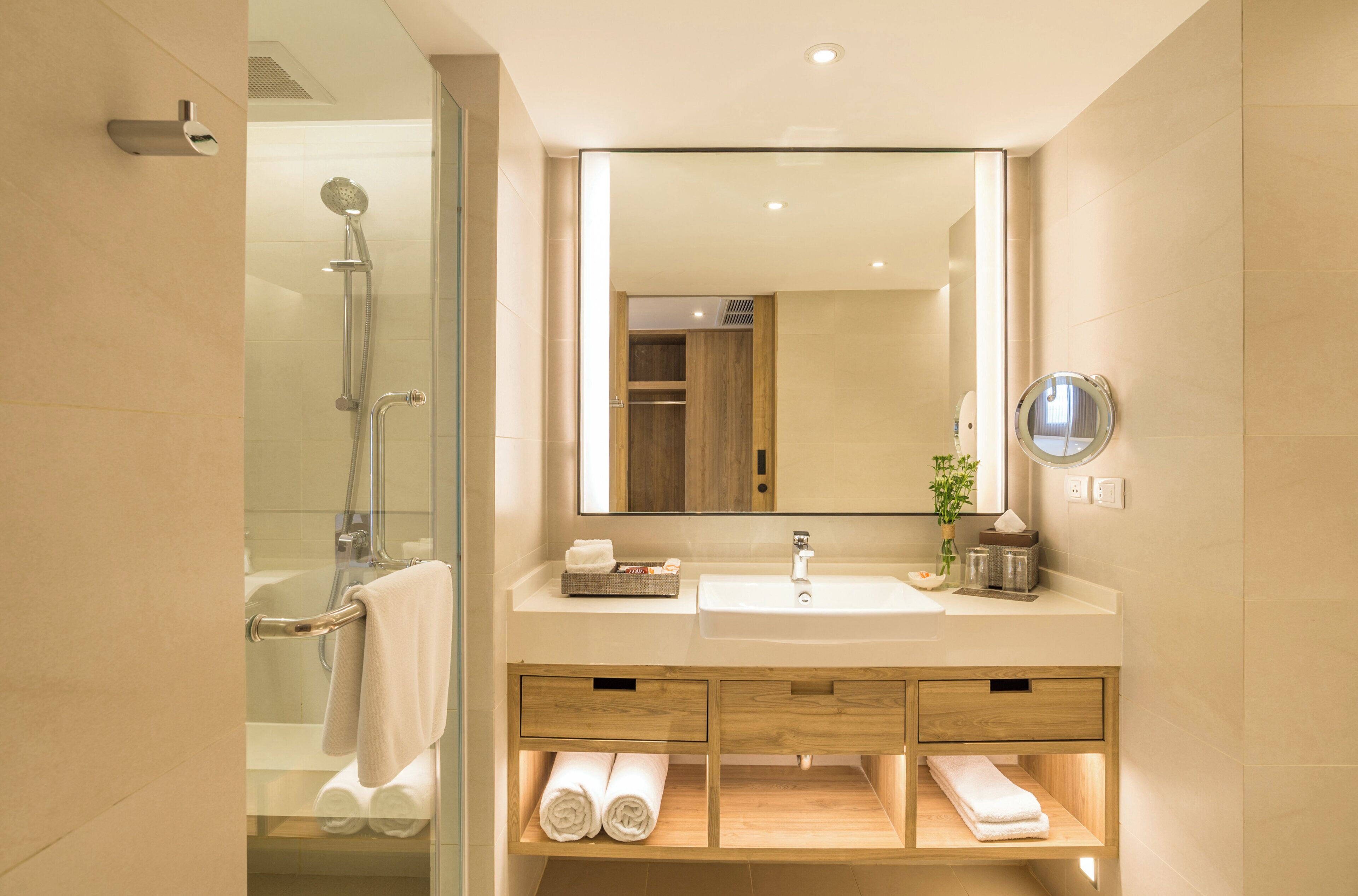 A modern bathroom with a glass-enclosed shower, a large mirror, and wooden vanity with built-in towel storage.