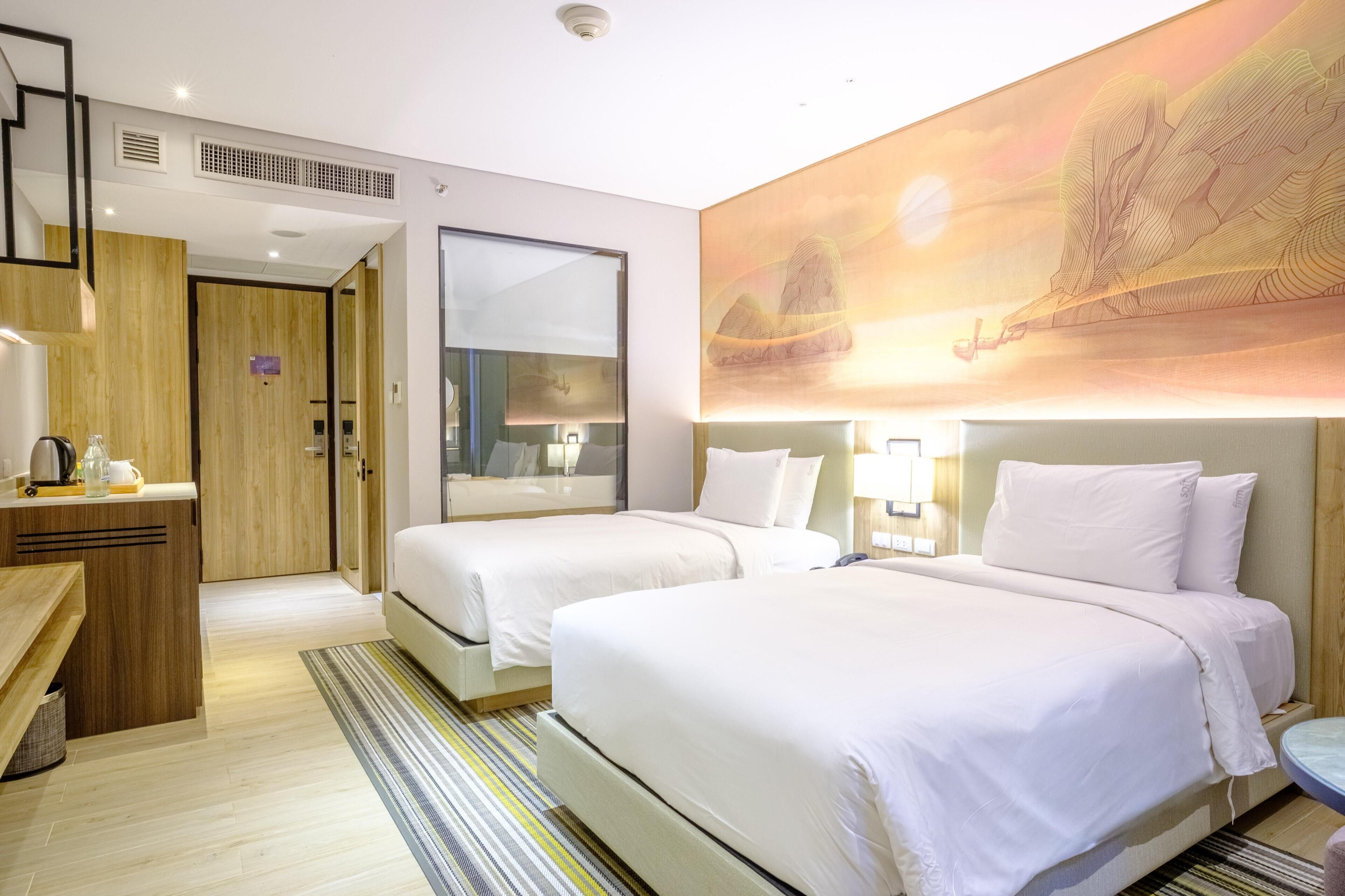 A hotel room with two beds, a desk, a mirror, and a large painting on the wall.