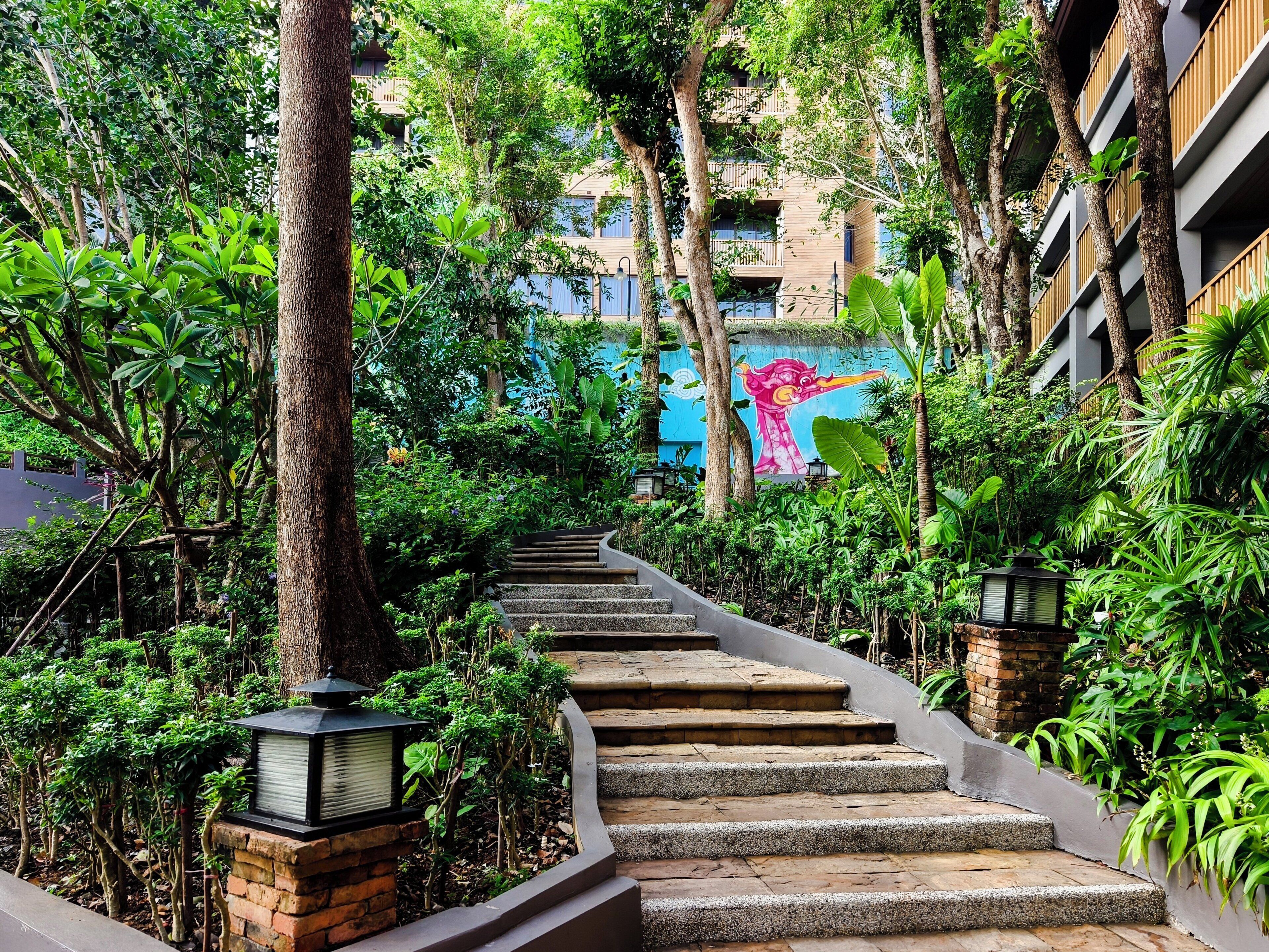 A staircase surrounded by lush greenery, leading to a building with a mural.