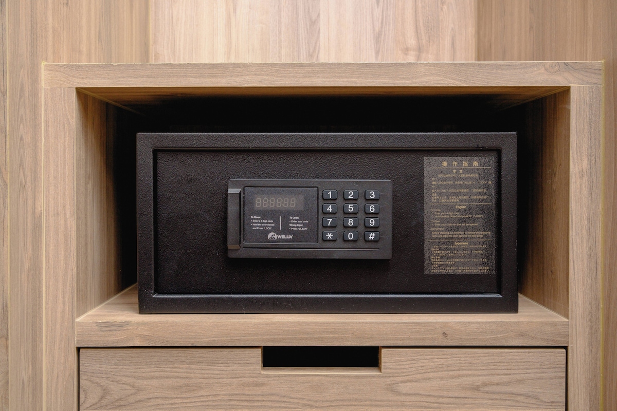 Una caja fuerte negra con teclado y pantalla, ubicada en un mueble de madera con un cajón debajo.