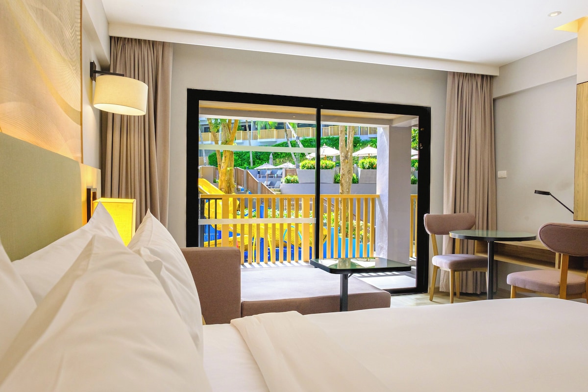 Une chambre d’hôtel avec un lit, un bureau et un balcon donnant sur un terrain de jeux.