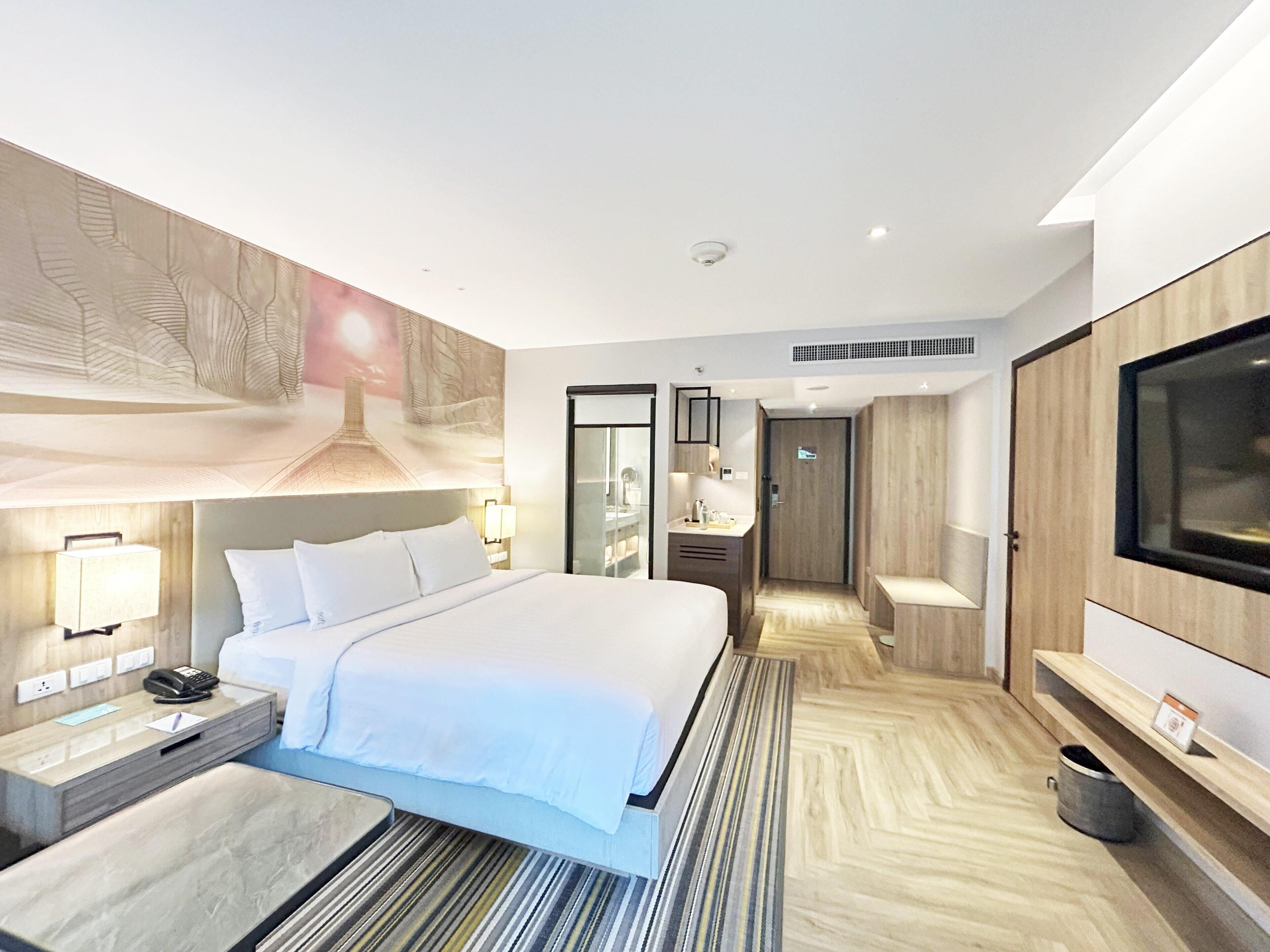 Una habitación de hotel moderna con una cama grande, mesitas de noche, televisión y vestidor.