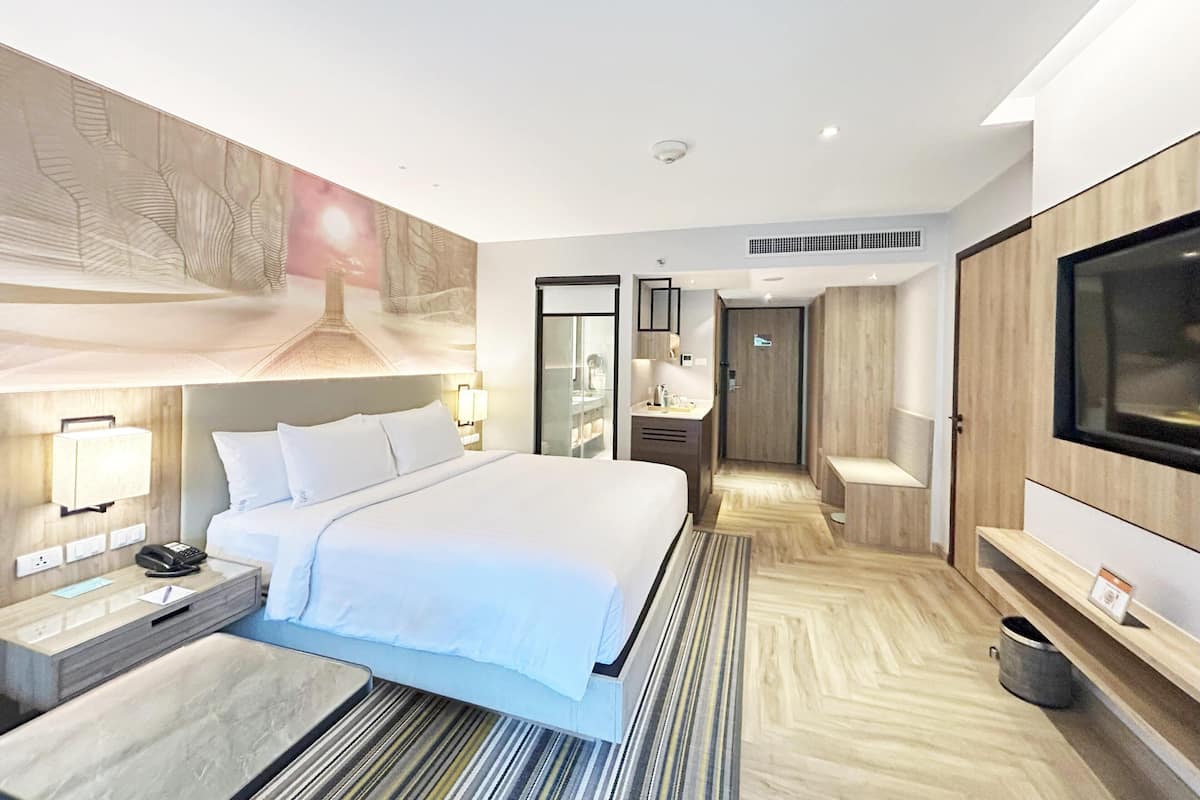 Una habitación de hotel moderna con una cama grande, mesitas de noche, televisión y vestidor.