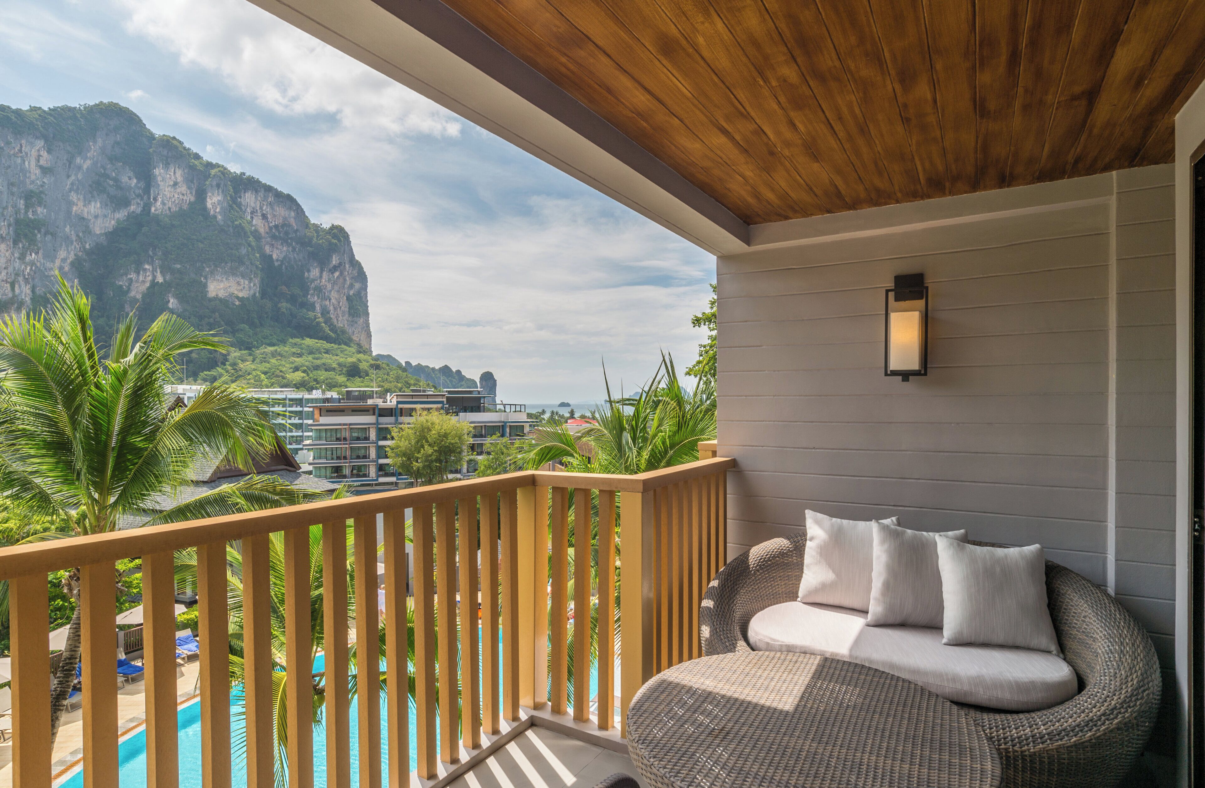 A balcony with a wicker sofa, a pool, and a view of a mountain.