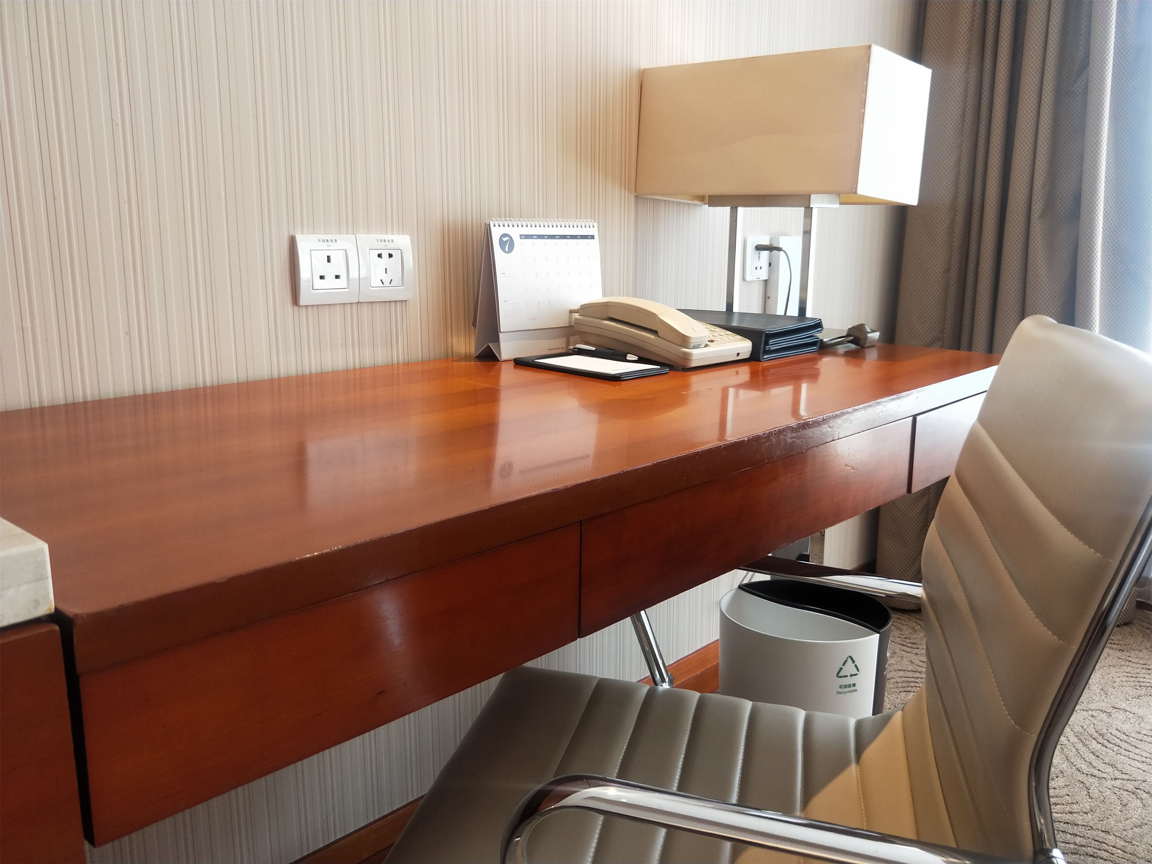 A hotel room desk with a telephone, lamp, and calendar.