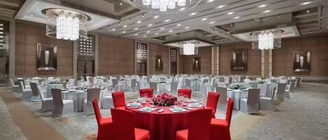 A large banquet hall with round tables, red and white chairs, and chandeliers.