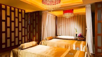 Two beds with matching headboards, adorned with decorative emblems, are set against a backdrop of a geometric-patterned partition and a chandelier.