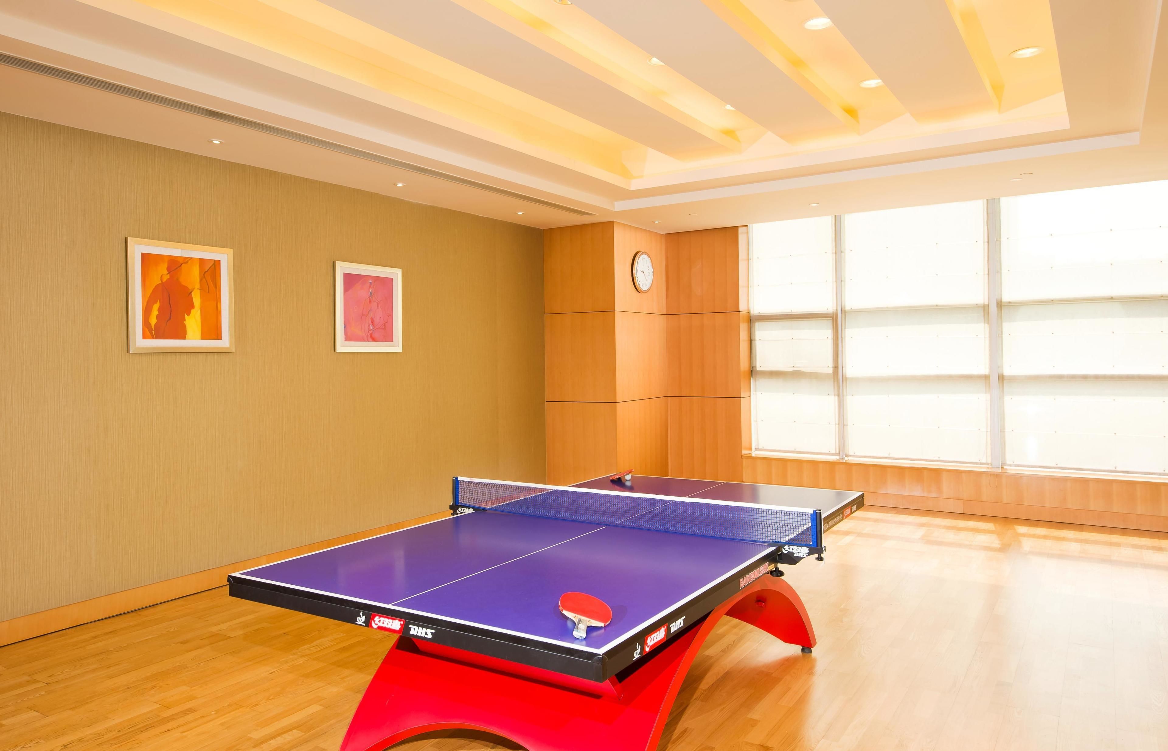 A ping pong table in a room with wooden flooring, beige walls, and two framed artworks.