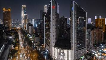 A nighttime cityscape with modern high-rise buildings, a busy street with moving vehicles, and illuminated signage.