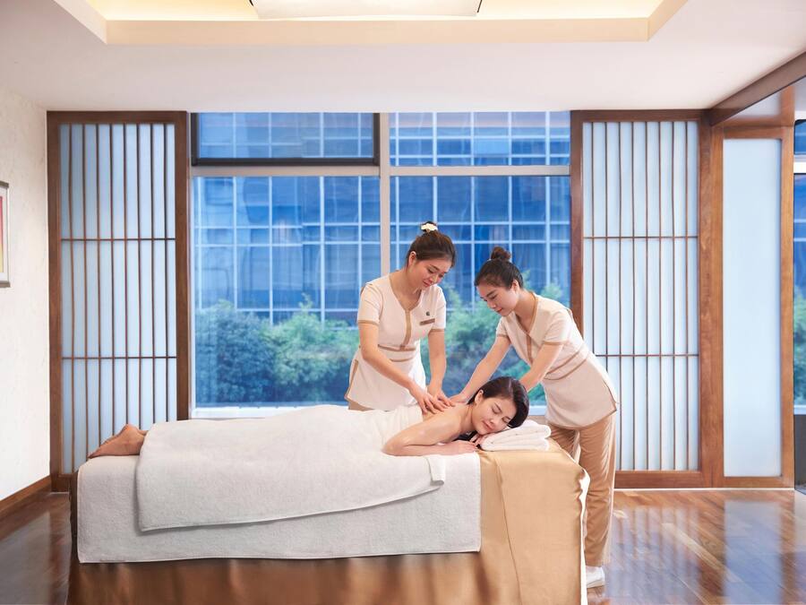 Ein Massageroom mit großem Fenster, Holzboden und einer Massageliege.