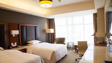 A hotel room with two beds, a desk, a chair, a small table, and a TV.