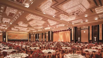 A large banquet hall with multiple round tables, each set with white tablecloths and red chairs.