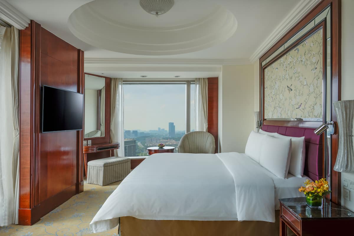 A hotel room with a large bed, a television, a desk, and a view of the city.