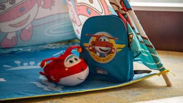 A blue backpack with a cartoon character and the words "SUPER WINGS" on it, placed on a blue mat with a toy fish beside it.