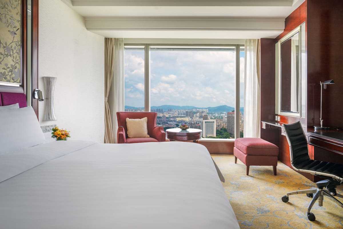 A hotel room with a large bed, a desk, a chair, and a view of the city.