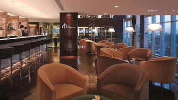 Un espace bar au design moderne, comprenant un comptoir, un coin salon avec des chaises et une vue sur la ville grâce à de grandes fenêtres.