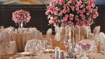 Una sala da banchetto con tavoli rotondi apparecchiati per un evento formale, con centrotavola floreali e una mise en place elegante.